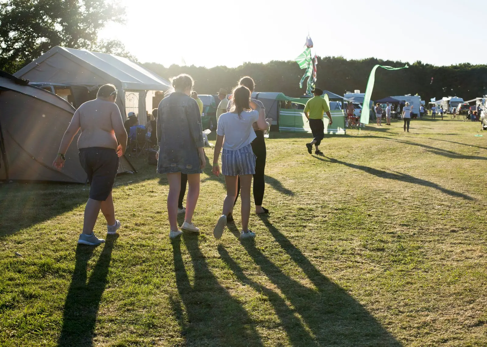 Rally-goers walking between tents and caravans in evening sunlight
